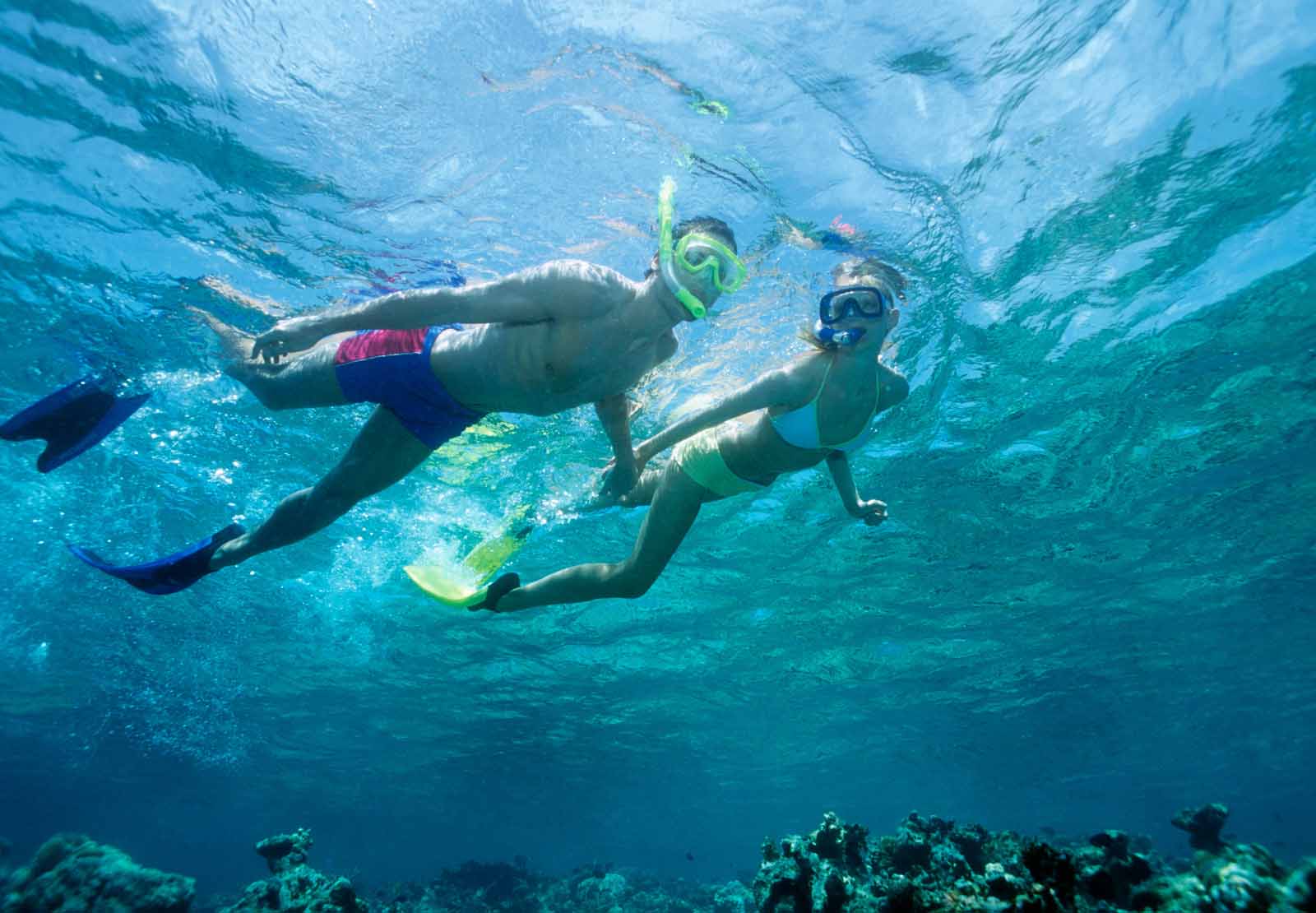 Young couple snorkelling above a shallow reef, underwater view.